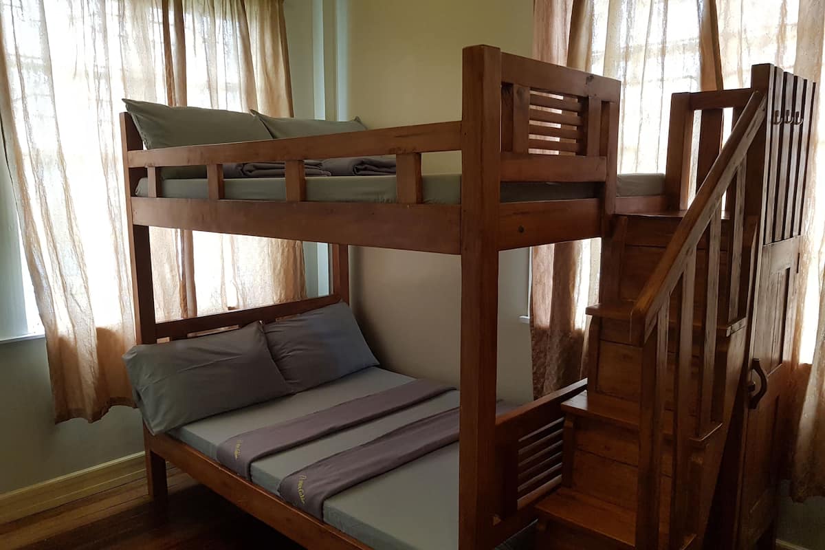 Una cama litera con estructura de madera, una cama inferior con almohadas y una escalera.