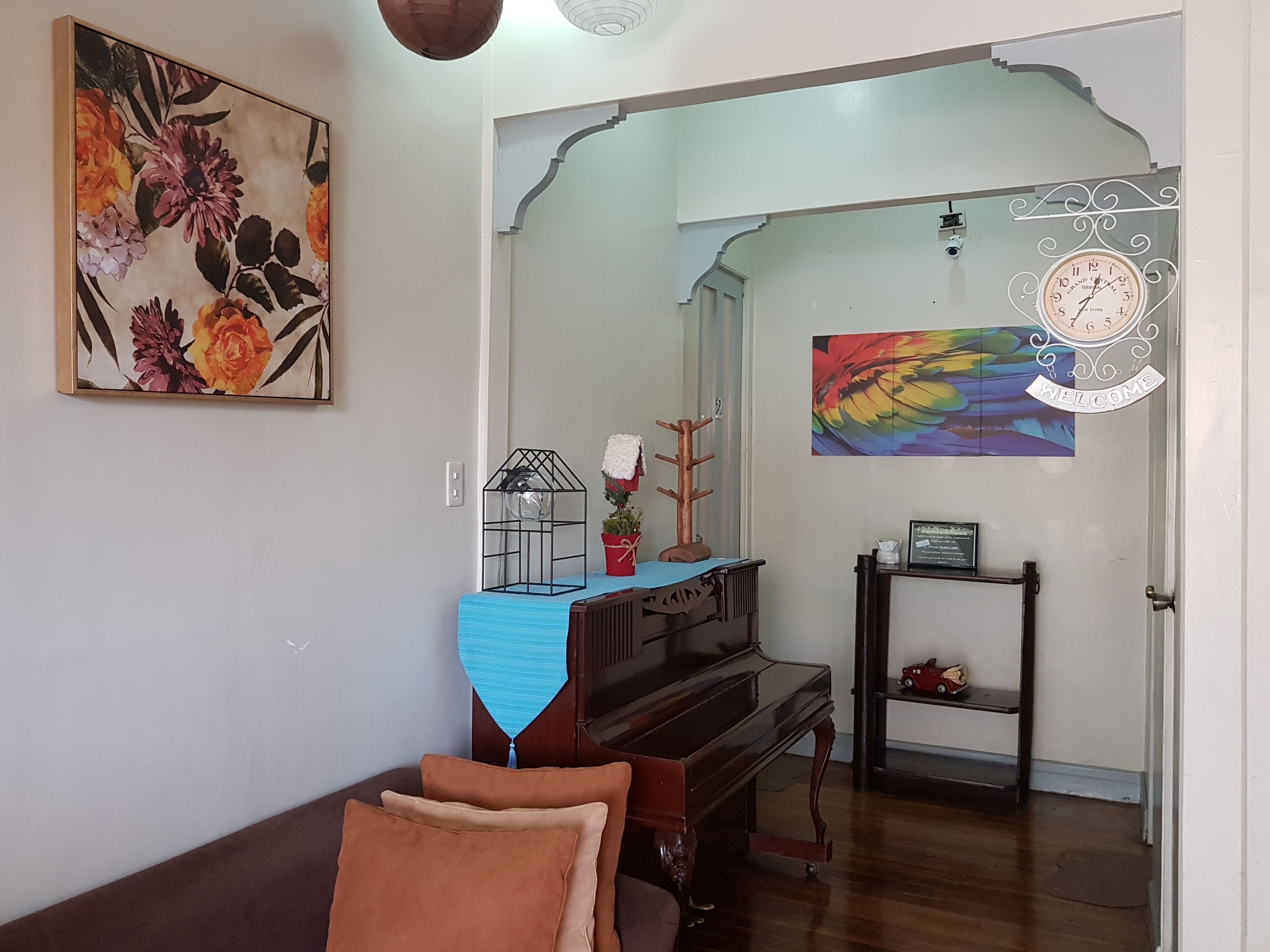 A living room with a piano, a couch, a wall-mounted clock, and a floral painting.