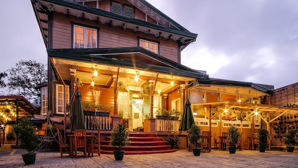 A two-story building with a porch, outdoor seating, and potted plants. - Elmar Cabin (Baguio)