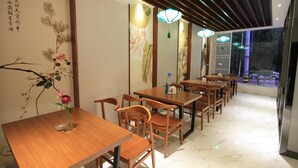 A restaurant with wooden tables and chairs, a vase with flowers, and traditional wall art. - Huangshan Castle In The Sky Hotel (Huangshan)