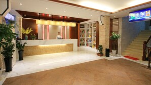 A hotel reception area with a marble floor, a reception desk, a TV screen, and a staircase. - Huangshan Castle In The Sky Hotel (Huangshan)
