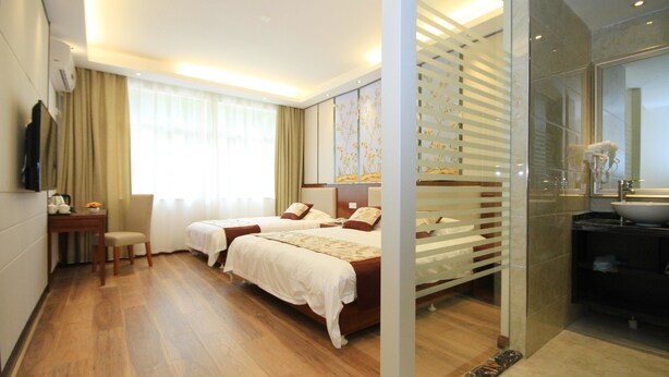A hotel room with two beds, a desk with a chair, a TV, and a bathroom with a sink and mirror. - Huangshan Castle In The Sky Hotel (Huangshan)