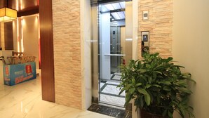 An elevator entrance with a marble floor, a potted plant, and a blue box with red text. - Huangshan Castle In The Sky Hotel (Huangshan)