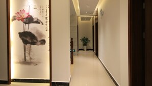 A hallway with a traditional painting on the left wall, a potted plant in the center, and a wooden door on the right. - Huangshan Castle In The Sky Hotel (Huangshan)