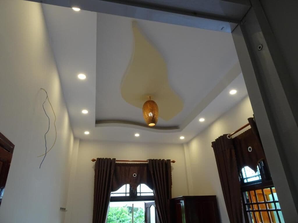 Une pièce avec un plafond haut, des spots encastrés, un luminaire suspendu et une fenêtre avec des rideaux.