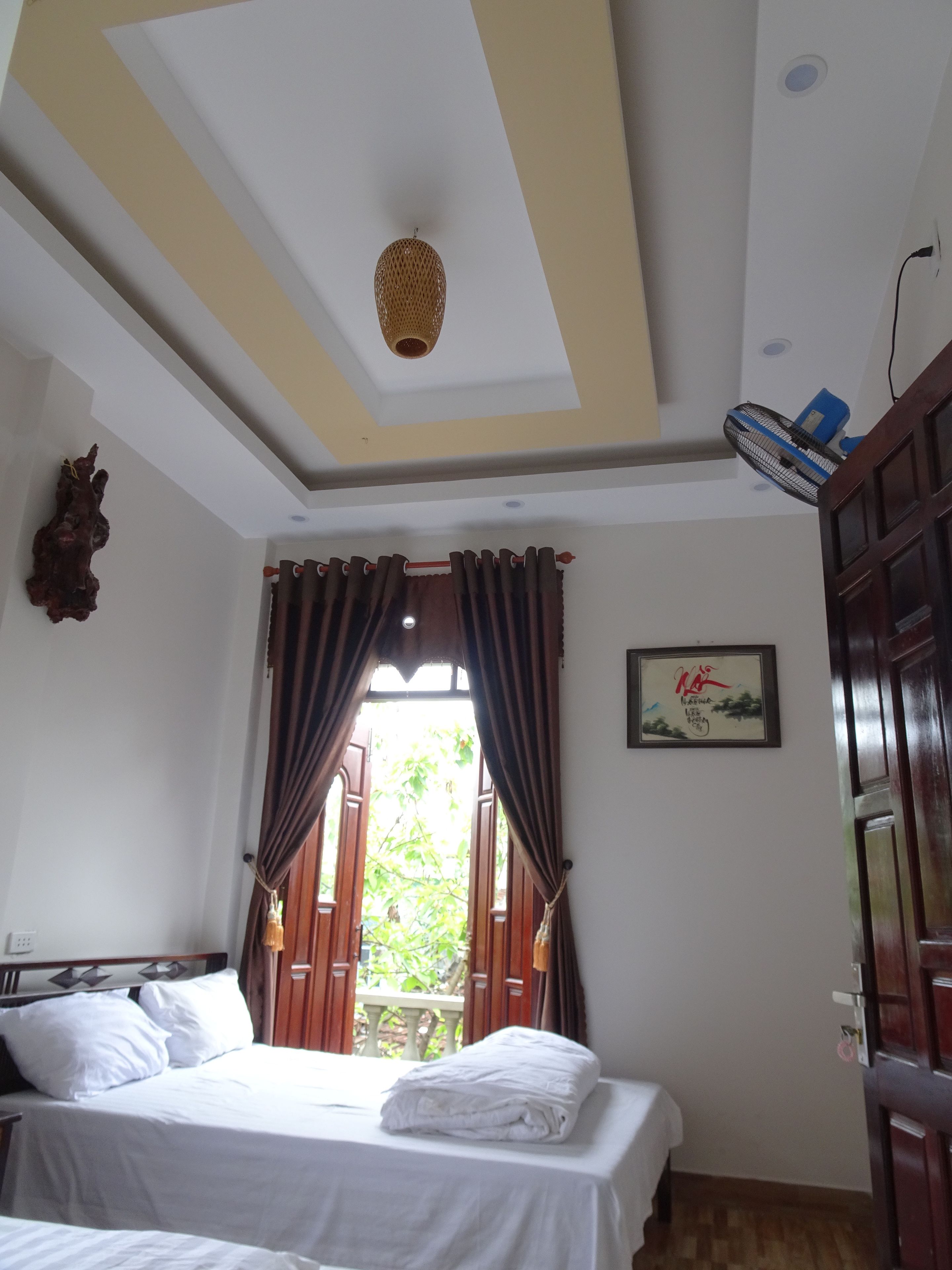 Une chambre à coucher avec un lit, des rideaux, un ventilateur de plafond et un tableau accroché au mur.