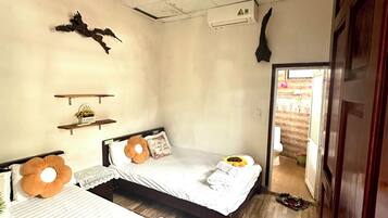 A hotel room with two beds, a ceiling fan, an air conditioning unit, a wall-mounted decoration, and a wooden floor.