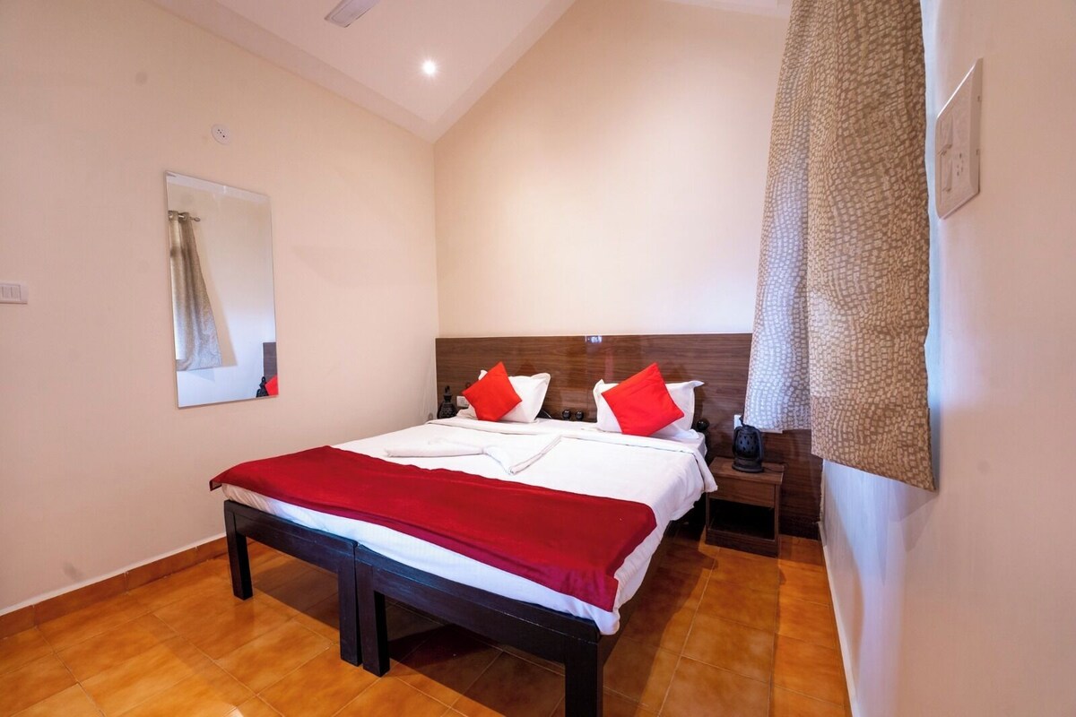 Ein Hotelzimmer mit einem großen Bett, zwei Nachttischen, einem Holzkopfende, einem Spiegel und einem gemusterten Vorhang.