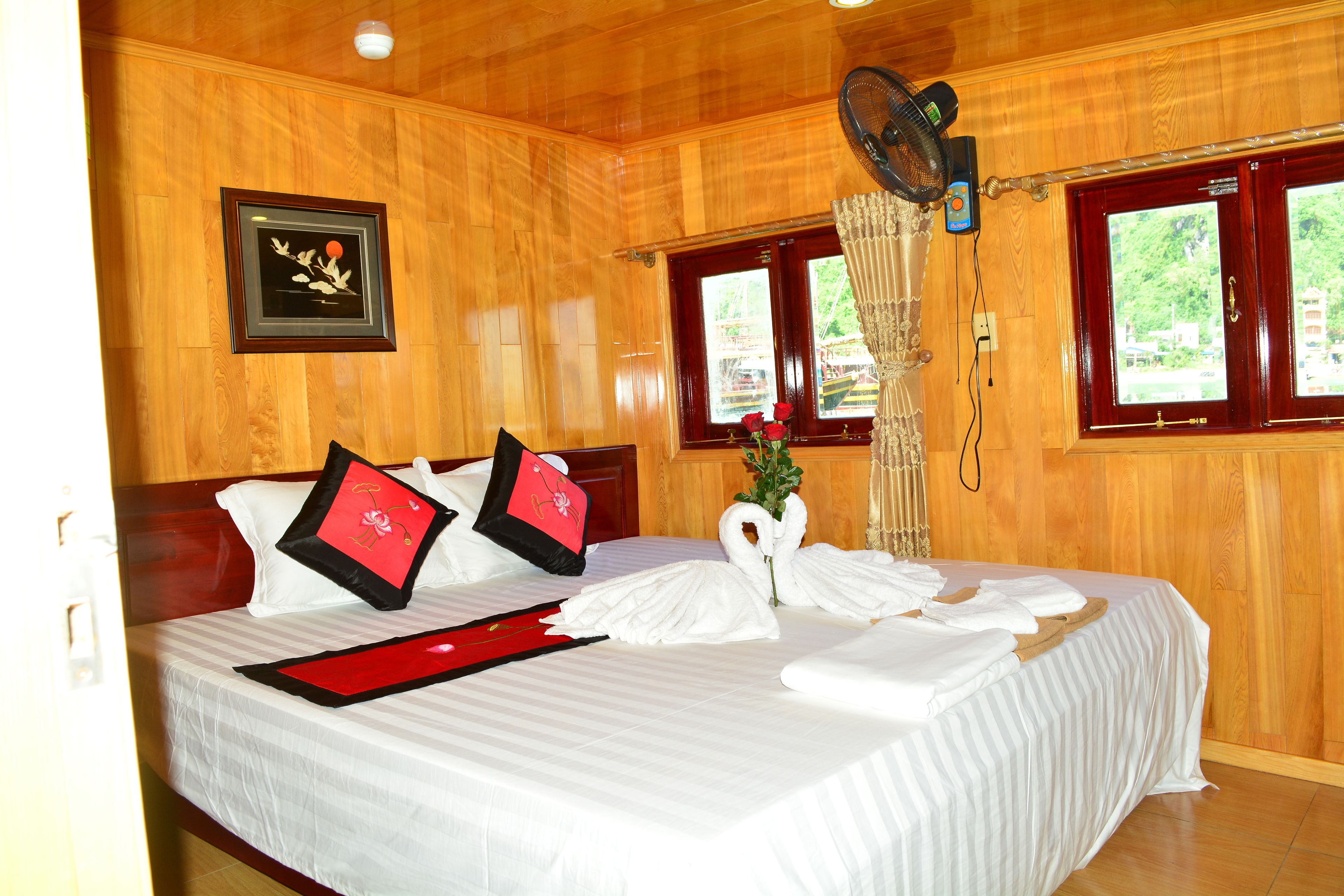 A neatly made bed with white bedding and red pillows, a framed picture on the wall, and a window with curtains.