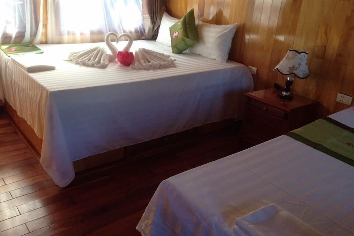 A hotel room with two beds, wooden flooring, and a nightstand with a lamp.