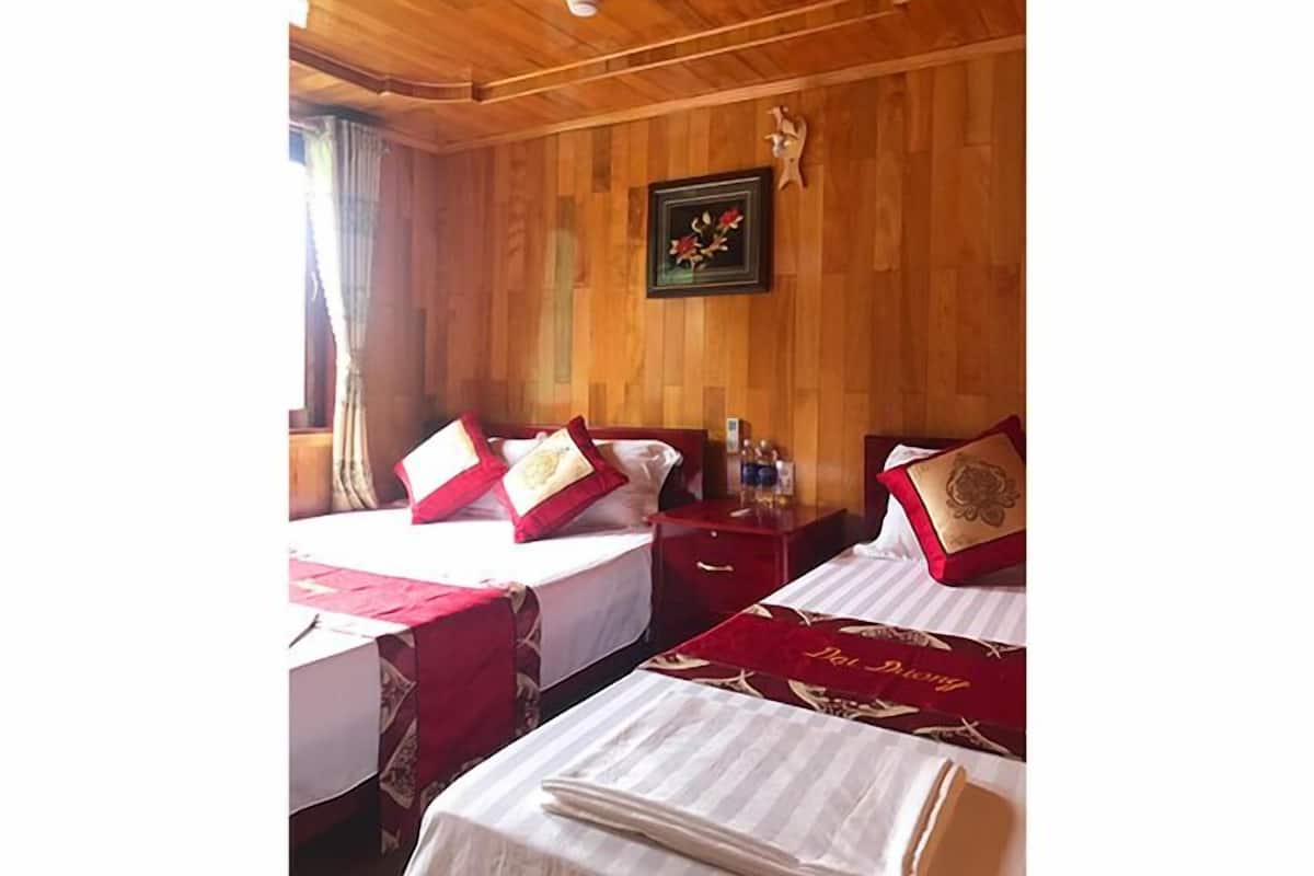 A wooden-paneled room with two beds, each with red and white bedding and a decorative pillow. A small table and a nightstand are visible, along with a framed picture on the wall.