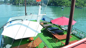 A boat with a green deck, wooden lounge chairs, and a red umbrella. - Ocean Cruise (Hai Phong)