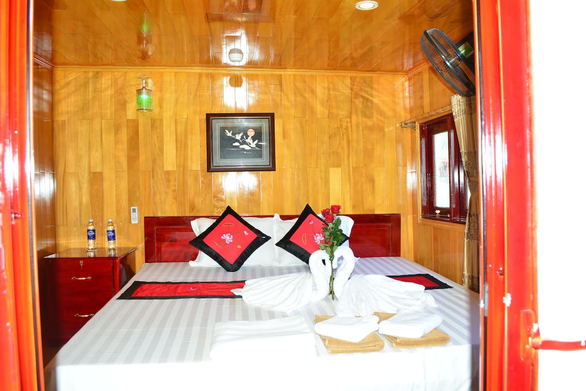 A hotel room with a wooden ceiling, a bed with white linens, red pillows, and a bouquet of roses.