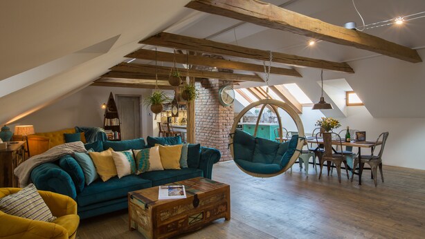 Un salón estilo loft con vigas de madera a la vista, un sillón colgante, un conjunto de sofás y un comedor con mesa y sillas.
