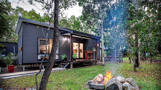 A modern house with a deck, a fire pit, and a well-maintained lawn. - Airlie Beach Eco Cabins - Adults only (Woodwark)