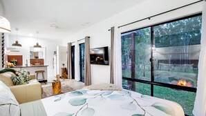 A modern bedroom with a large bed, a TV, a kitchen area, and a view of a forest. - Airlie Beach Eco Cabins - Adults only (Woodwark)