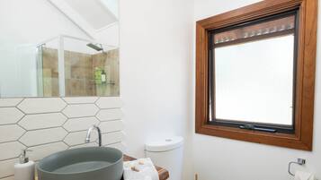 A bathroom with a hexagonal tile backsplash, a round sink, a wooden countertop, a toilet, and a window with a wooden frame.