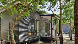 A modern cabin with a large sliding glass door, a covered porch, and a dirt ground with scattered leaves. - Airlie Beach Eco Cabins - Adults only (Woodwark)