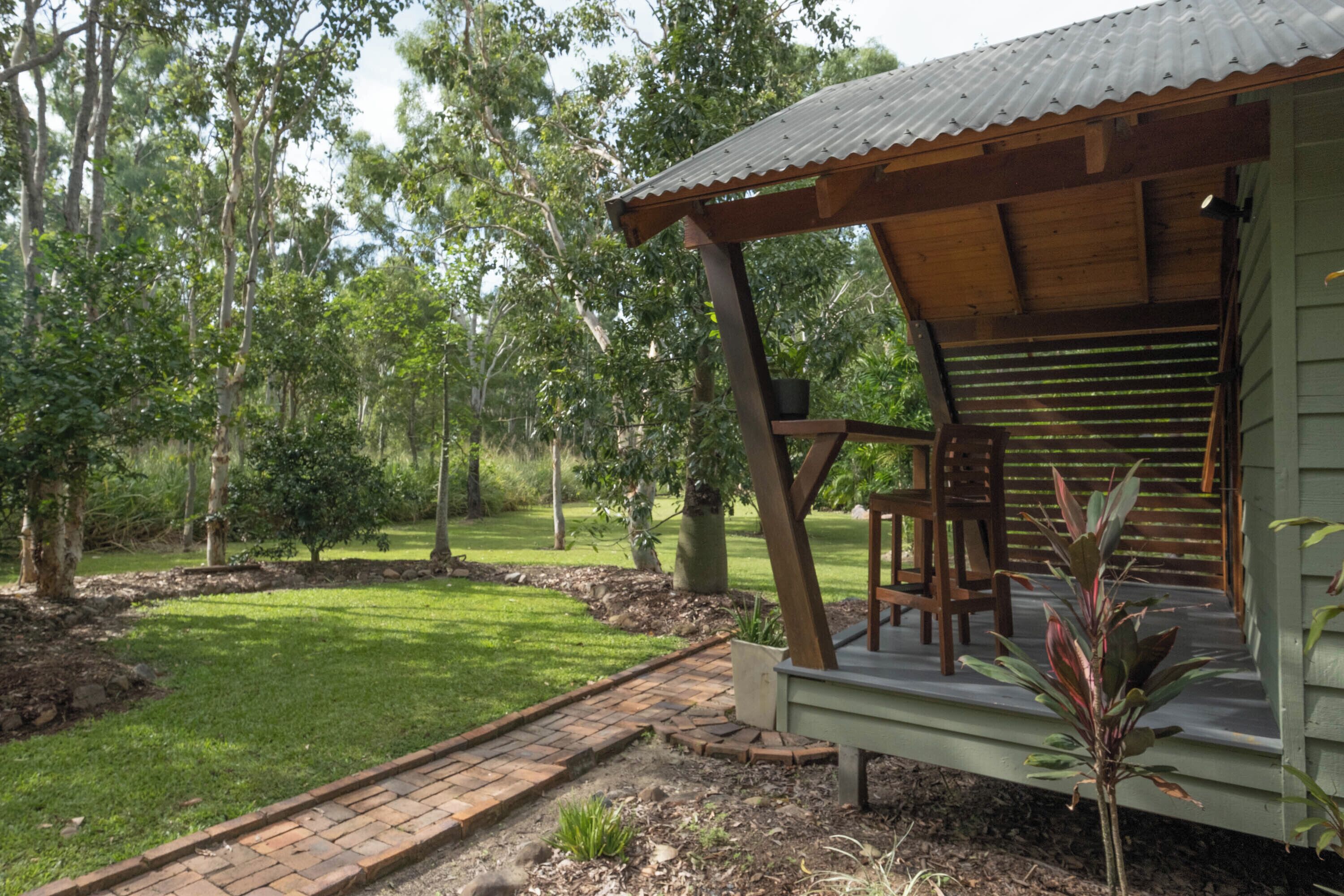 A wooden deck with a metal roof, surrounded by a garden with a brick pathway.