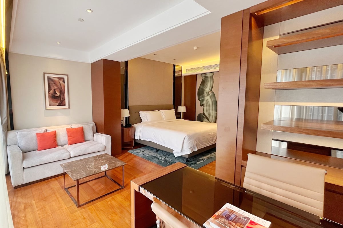 A hotel room with a bed, a sofa, a coffee table, a TV, and a bookshelf.