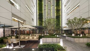 Een moderne hotelentree met een centraal zitgedeelte, verticale beplanting en een combinatie van binnen- en buitenruimtes.