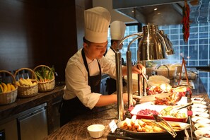 Montaje de bufé con diversas opciones de comida y un cocinero preparando platos.