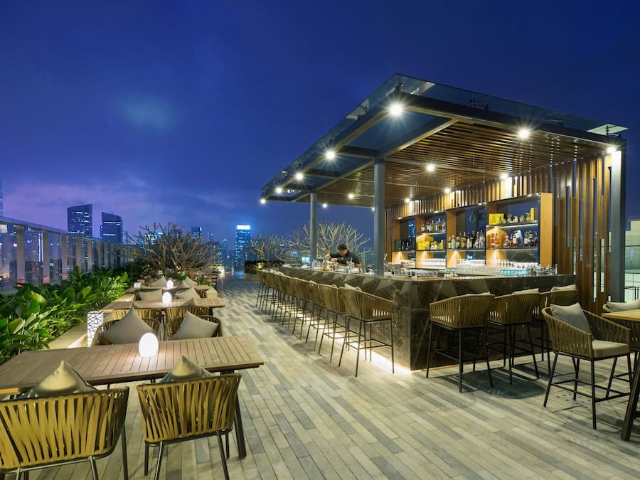 Zona de bar al aire libre con asientos y vista a la ciudad al atardecer.