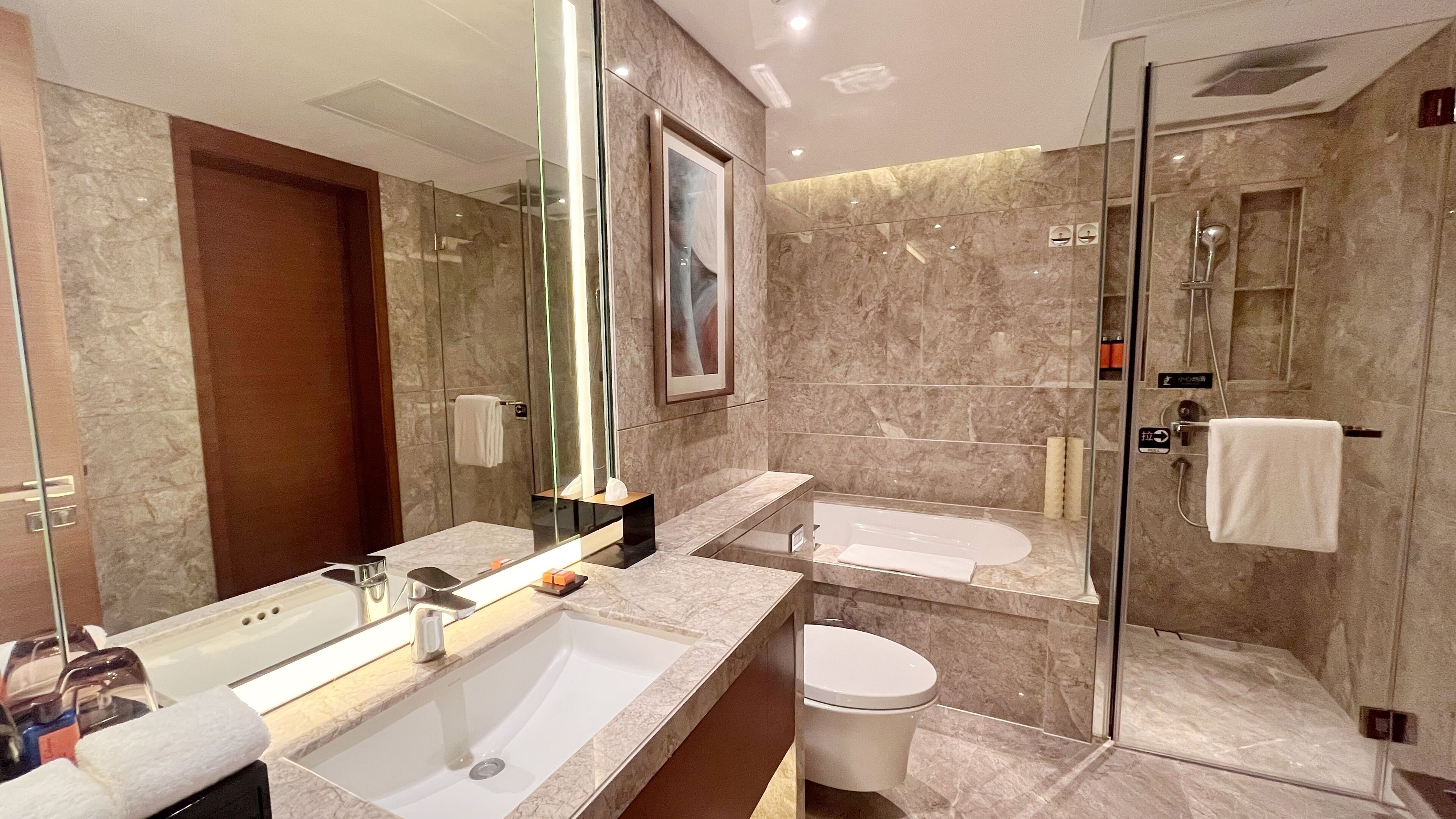 Un baño moderno con un espejo grande, un lavamanos, un inodoro y una zona de ducha.