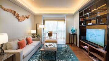 A modern living room with a sofa, coffee table, and TV. There is a bookshelf and a window with curtains.