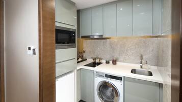 Een compacte keuken met een ingebouwde magnetron, een roestvrijstalen spoelbak en een wasmachine.