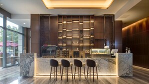 Een moderne bar met marmeren werkbladen, barkrukken en een goed verlichte presentatie van flessen en glazen.