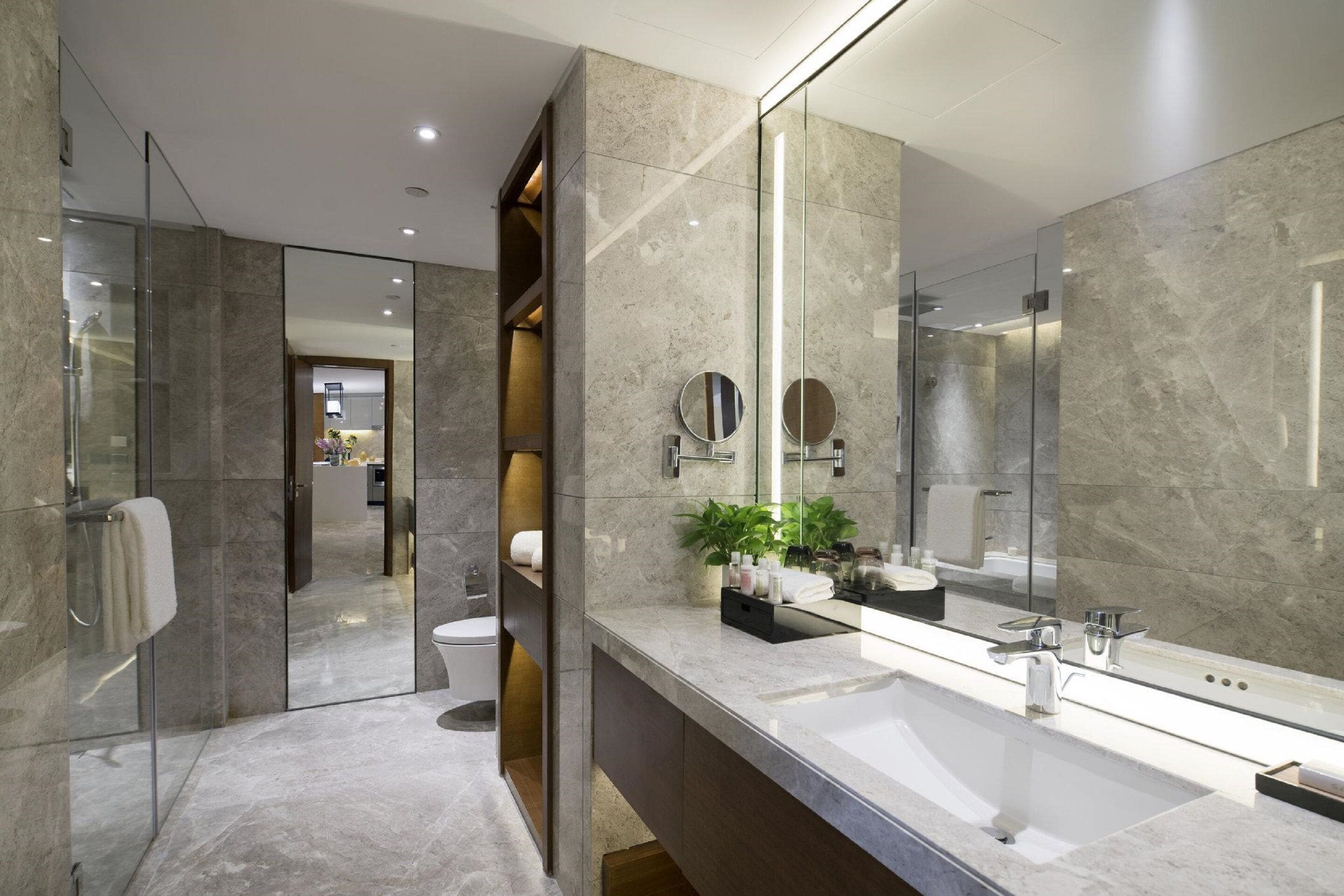 A modern bathroom with a large mirror, a glass shower enclosure, and a marble countertop.