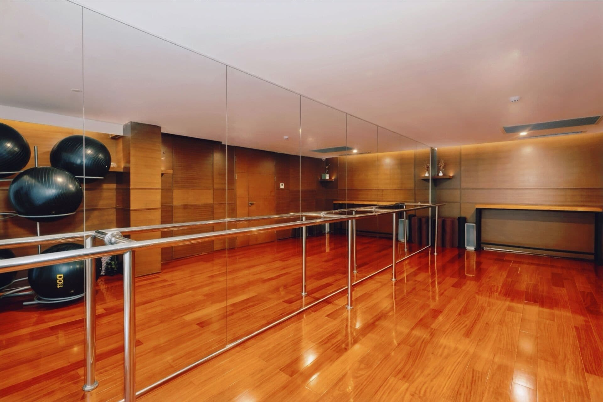 A spacious dance studio with wooden floors, mirrored walls, and exercise balls.