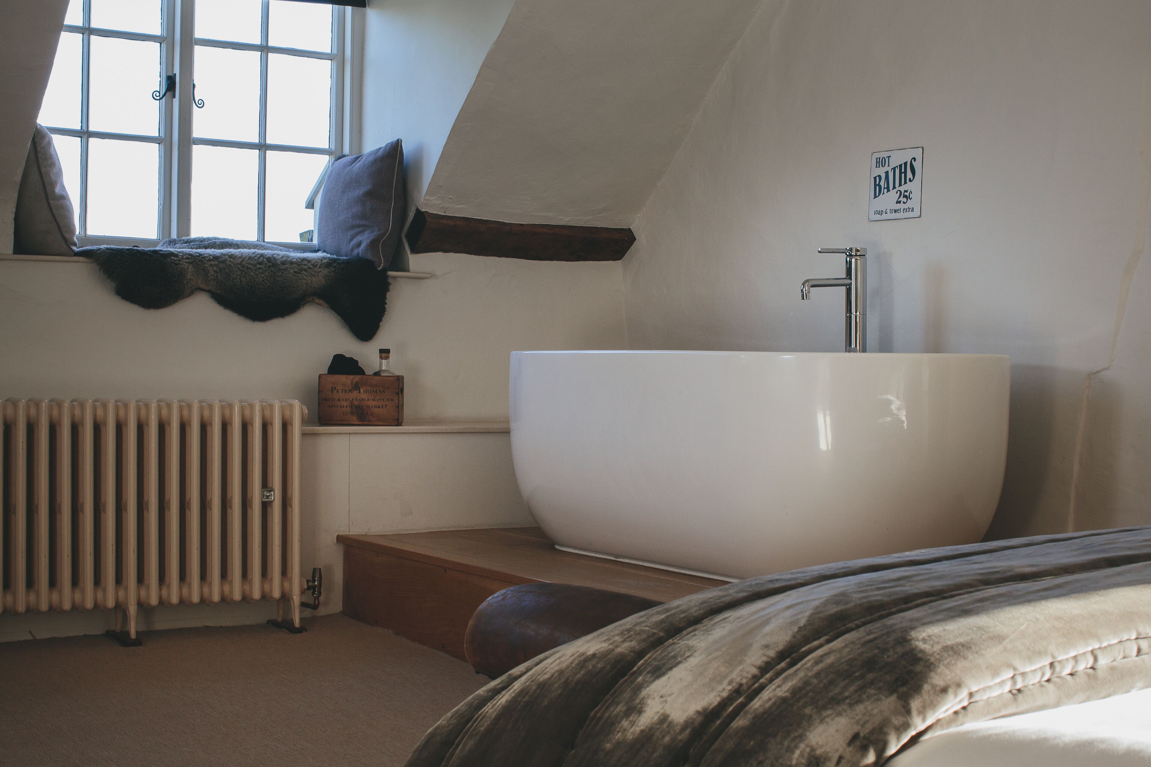A bathroom with a large bathtub, a window with a view, a radiator, and a sign indicating hot baths are available for 25 cents.