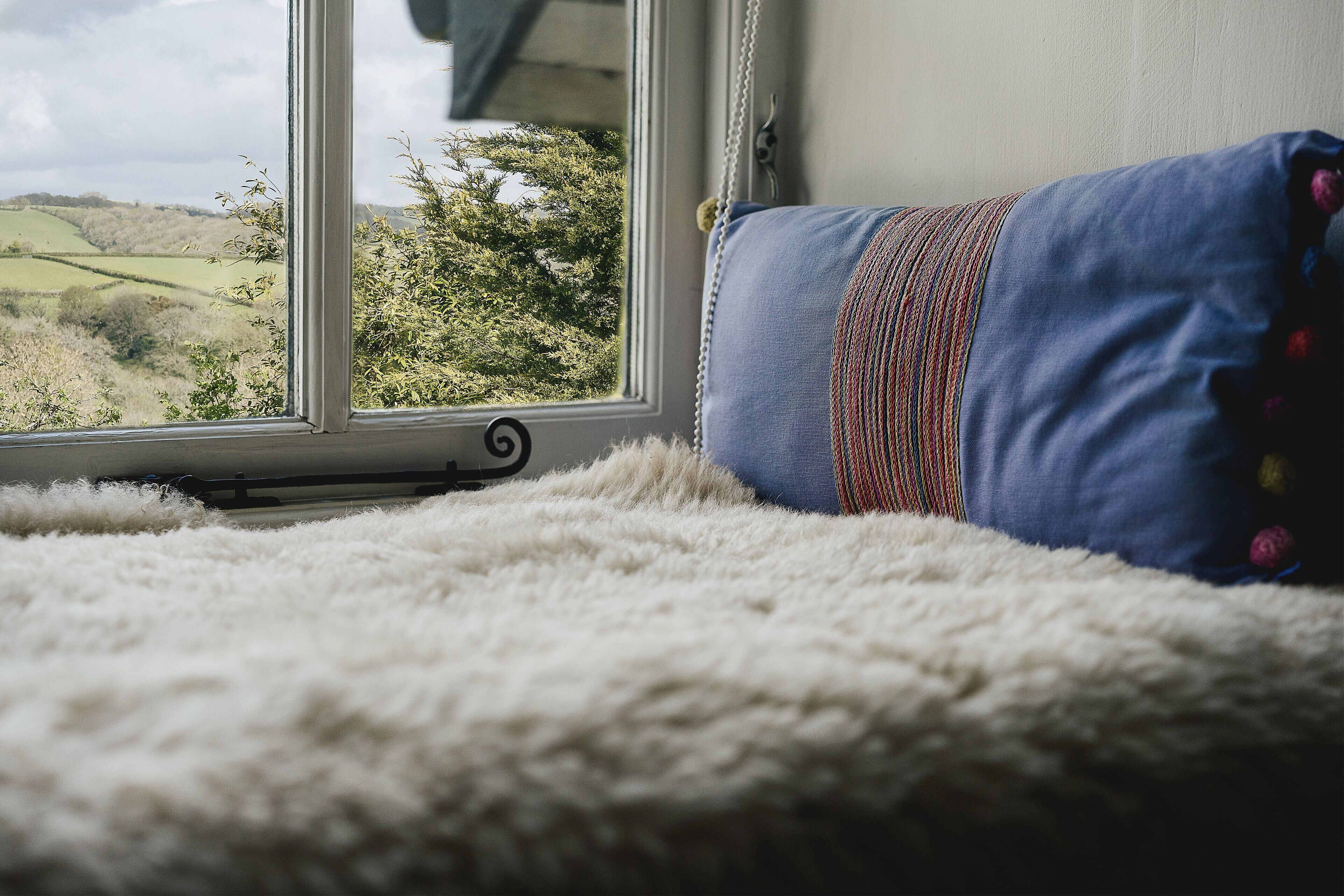 A bed with a view of a green landscape through a window.