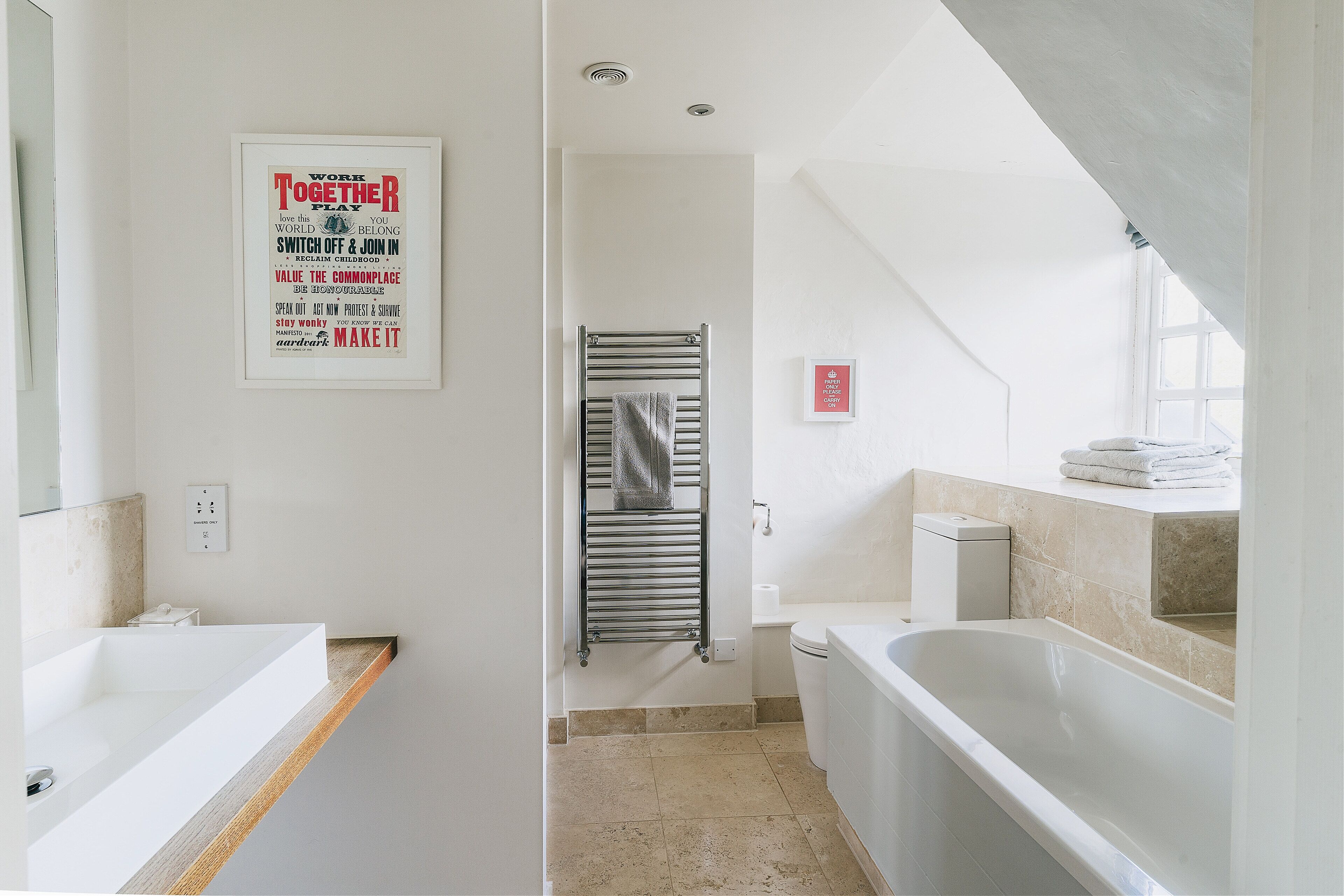 A modern bathroom with a bathtub, a shower, and a toilet. There are two framed posters on the wall.