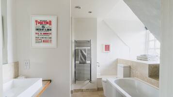 A modern bathroom with a bathtub, a shower, and a toilet. There are two framed posters on the wall.