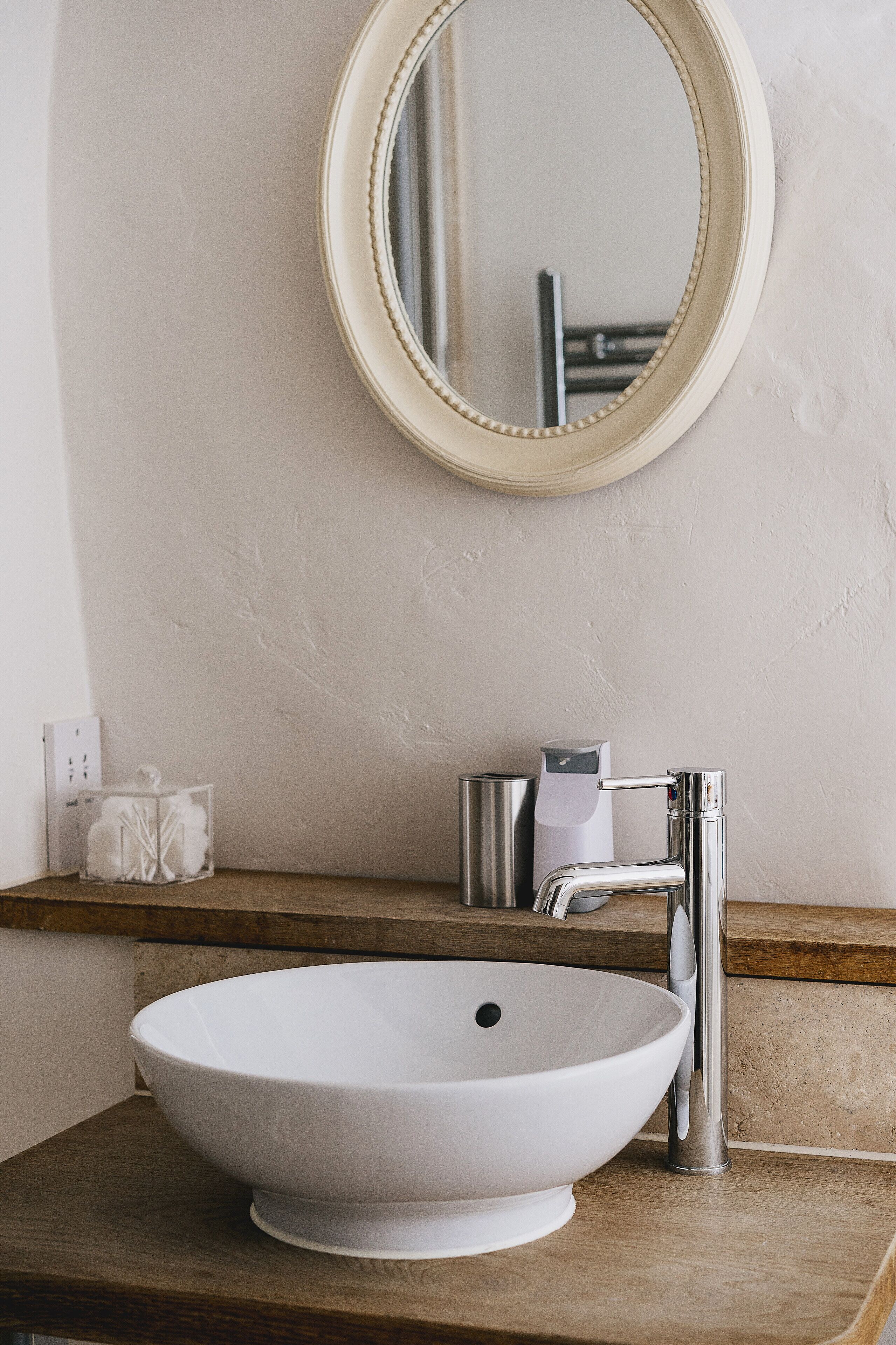 A bathroom with a white sink, a round mirror, and a chrome faucet.