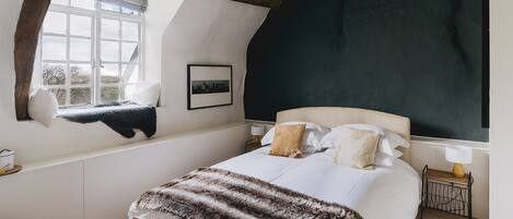 A bedroom with a large bed, a window with a view, a bedside table with a lamp, and a picture on the wall.