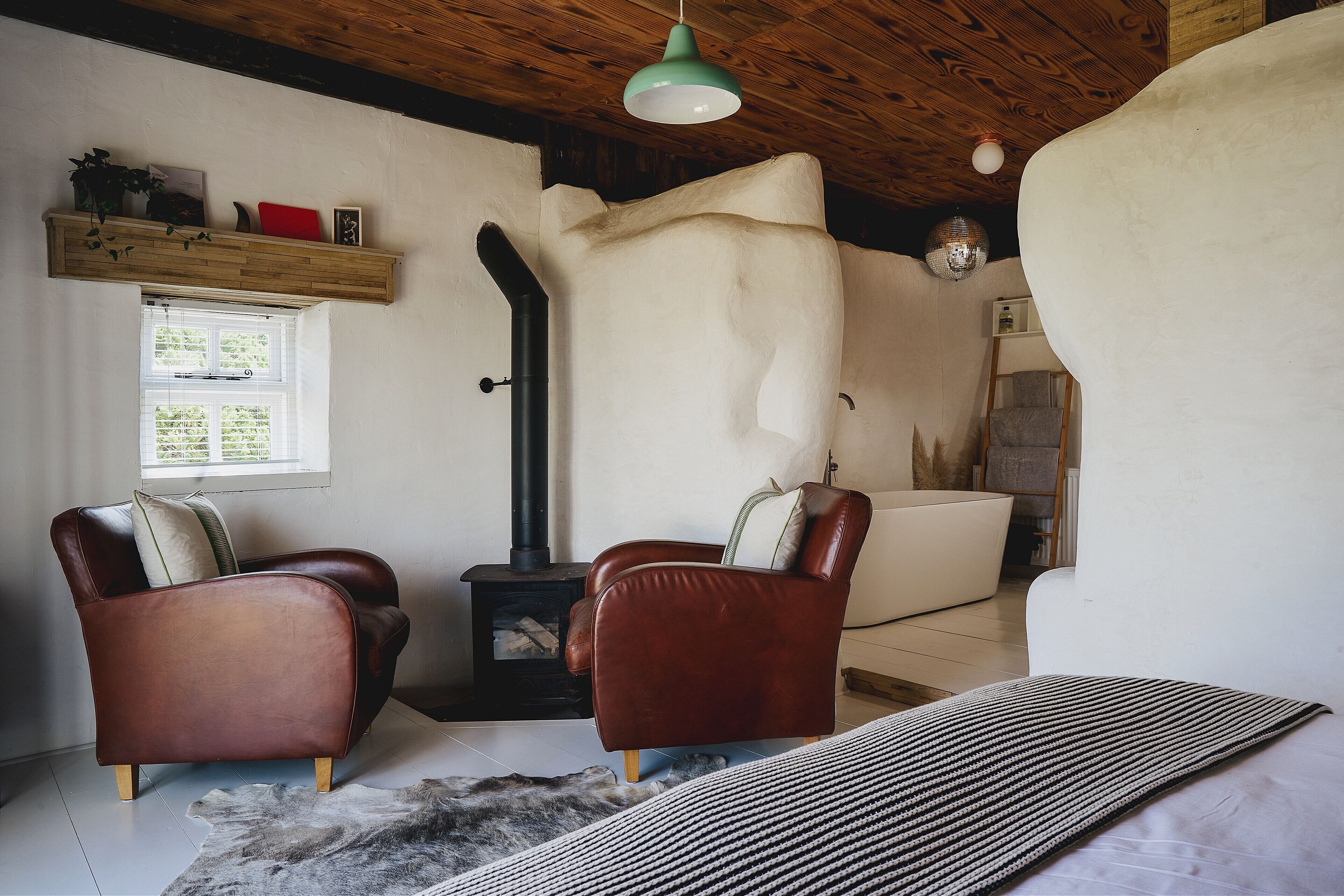 A cozy room with a fireplace, two leather armchairs, a sofa, and a hanging light fixture.
