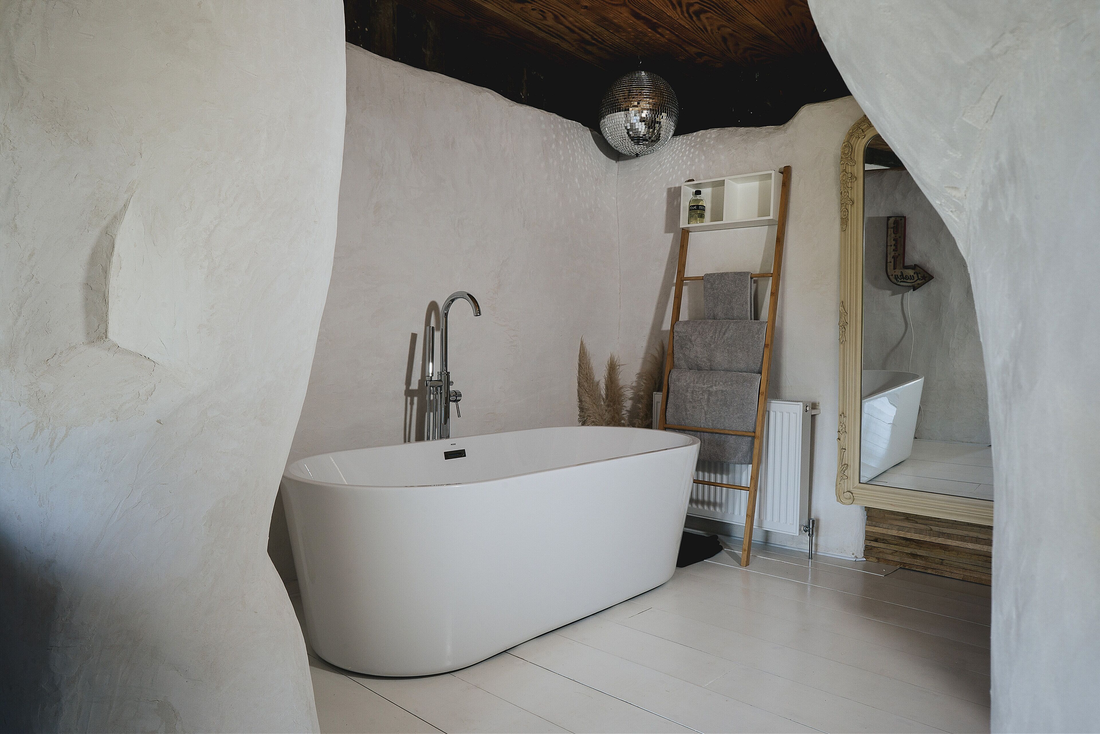A modern bathroom with a freestanding bathtub, a wooden ladder, a mirror, and a disco ball.