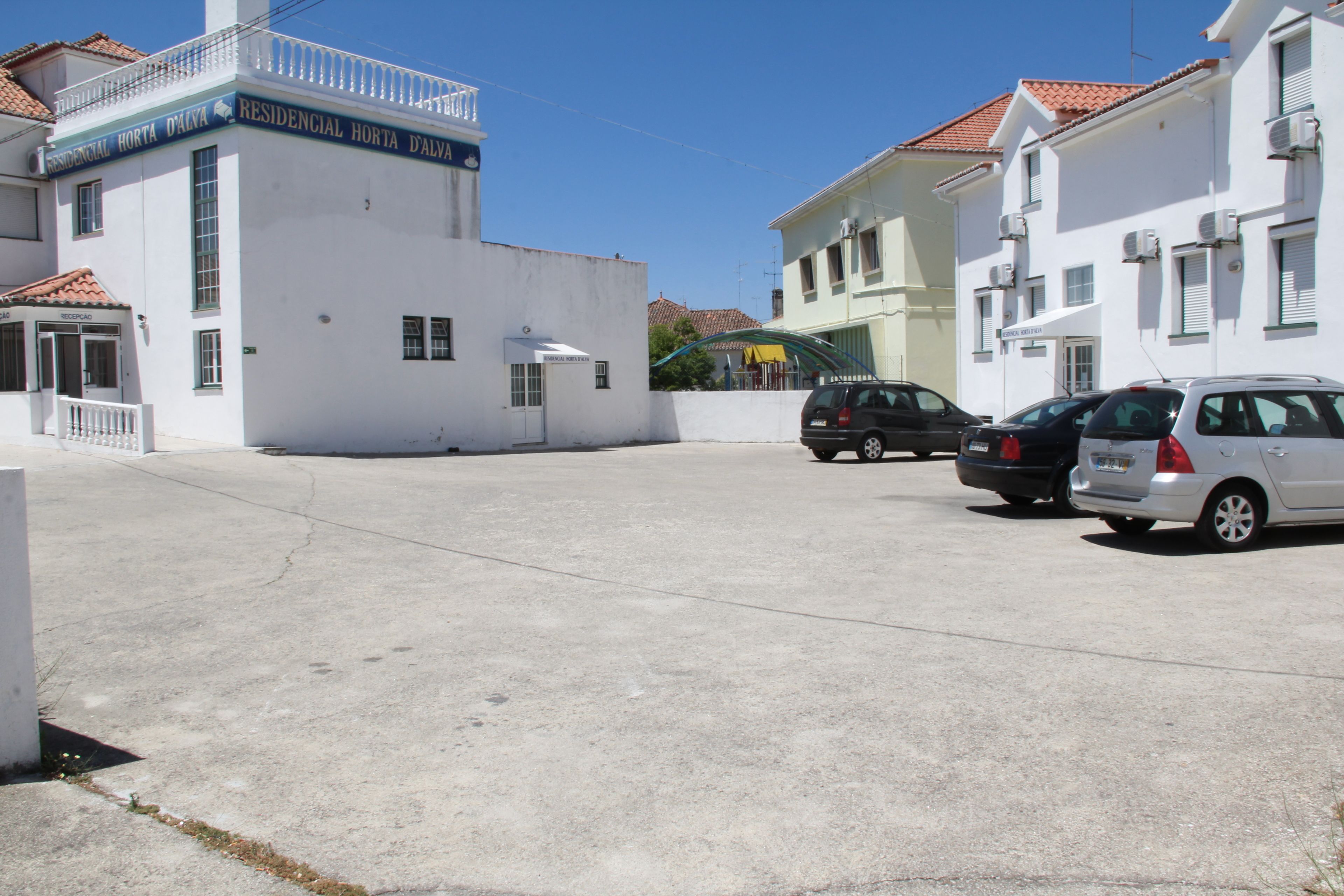 En boligbygning med et skilt, der siger "RESIDENCIAL HORTA D'ALVA". Der er biler parkeret foran, og bygningen har en balkon med gelænder.