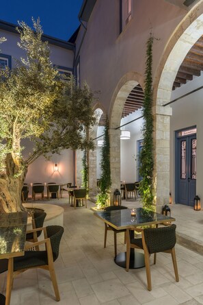 An outdoor dining area with tables and chairs, surrounded by stone arches and greenery. - S Paul Hotel (Limassol)