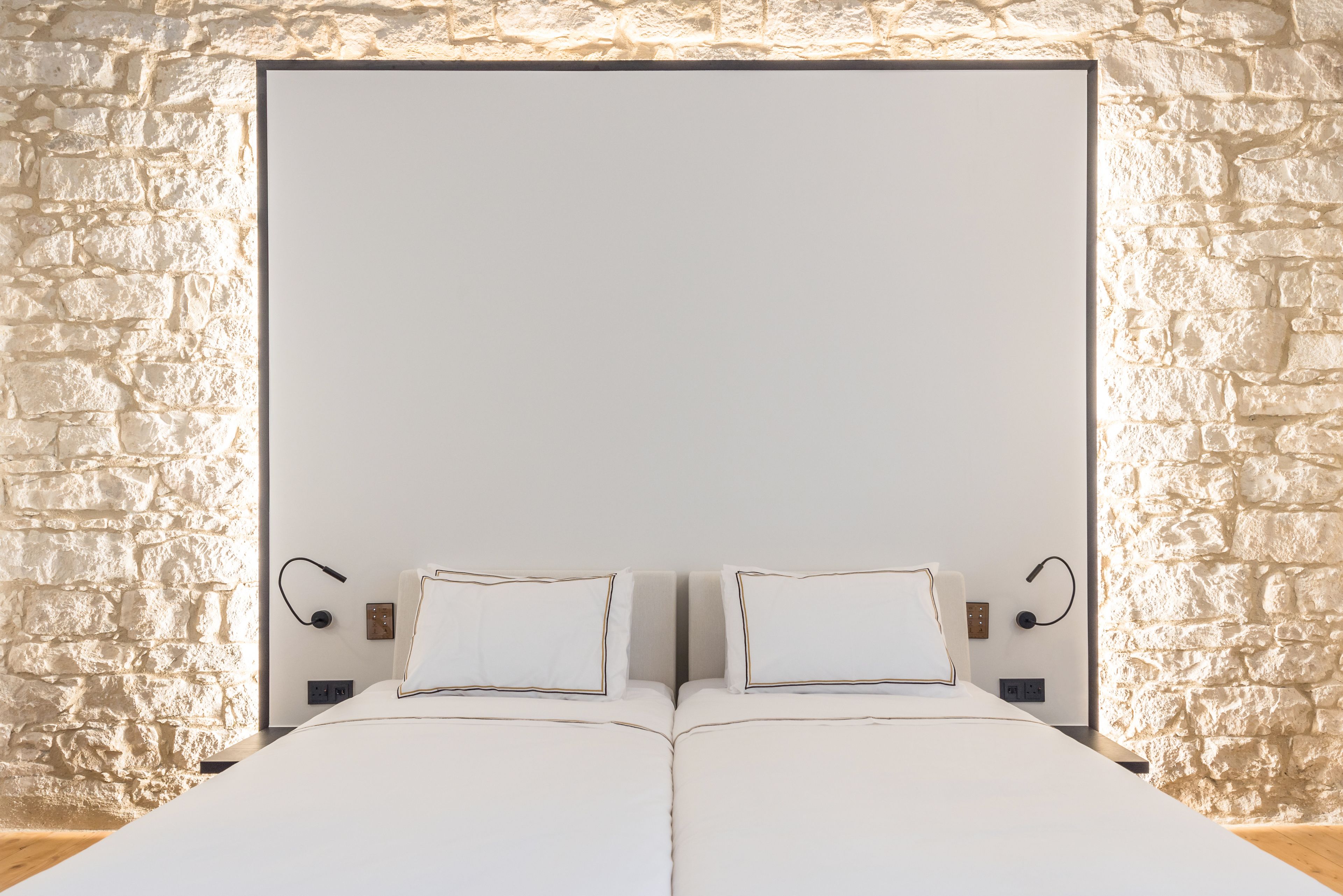 A double bed with white bedding and a headboard against a stone wall.