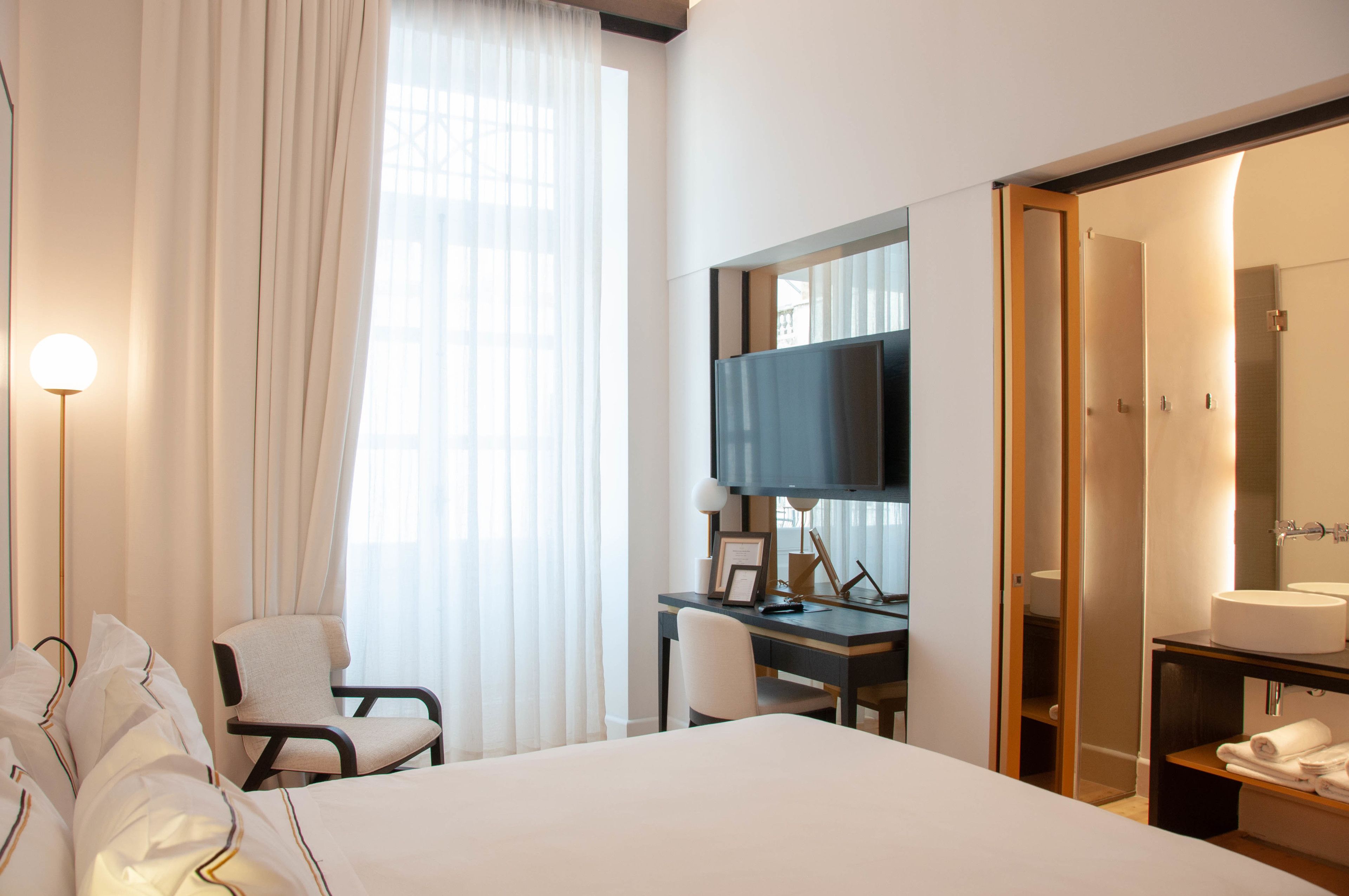 Ein Hotelzimmer mit einem Bett, einem Schreibtisch mit Computer, einem Fernseher und einem Badezimmer mit Waschbecken und Spiegel.