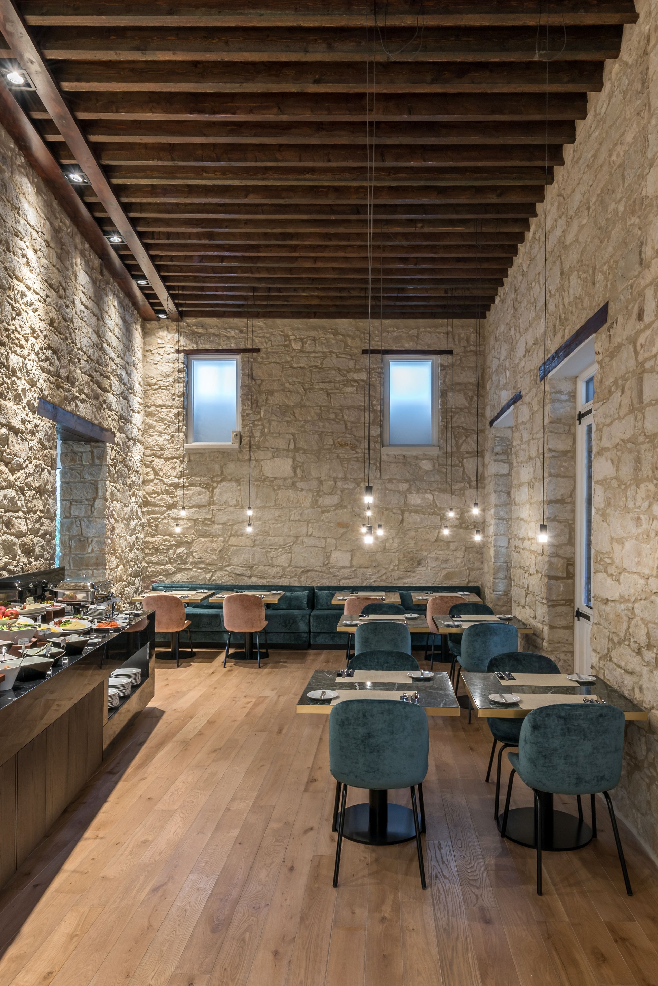 Un comedor rústico con paredes de piedra, vigas de madera y una variedad de opciones de asientos, incluyendo mesas y bancos.