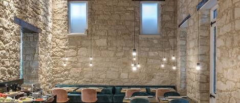 Un comedor rústico con paredes de piedra, vigas de madera y una variedad de opciones de asientos, incluyendo mesas y bancos.