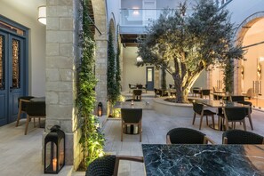 An outdoor dining area with stone walls, wooden furniture, and a tree. - S Paul Hotel (Limassol)