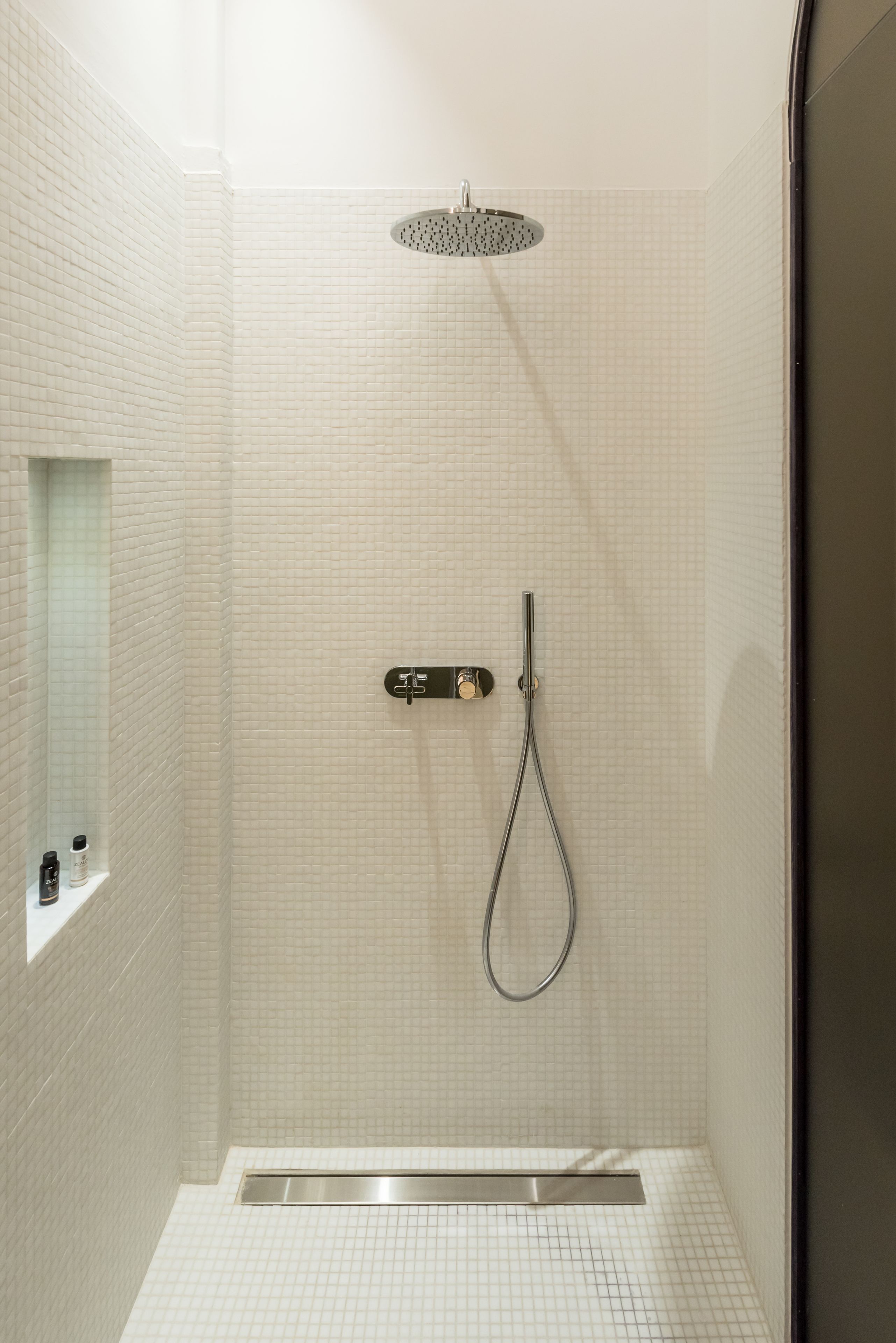 Una ducha a ras de suelo con cabezal de ducha de mano y panel de control en la pared.