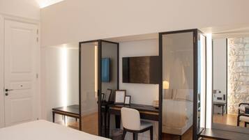 A hotel room with a bed, a desk with a chair, a TV mounted on the wall, and a stone wall.